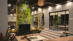 A modern living room with a large TV, a fireplace, and a green wall. There are steps leading to a balcony with outdoor seating. - Likha Wellness Resort (Lipa)