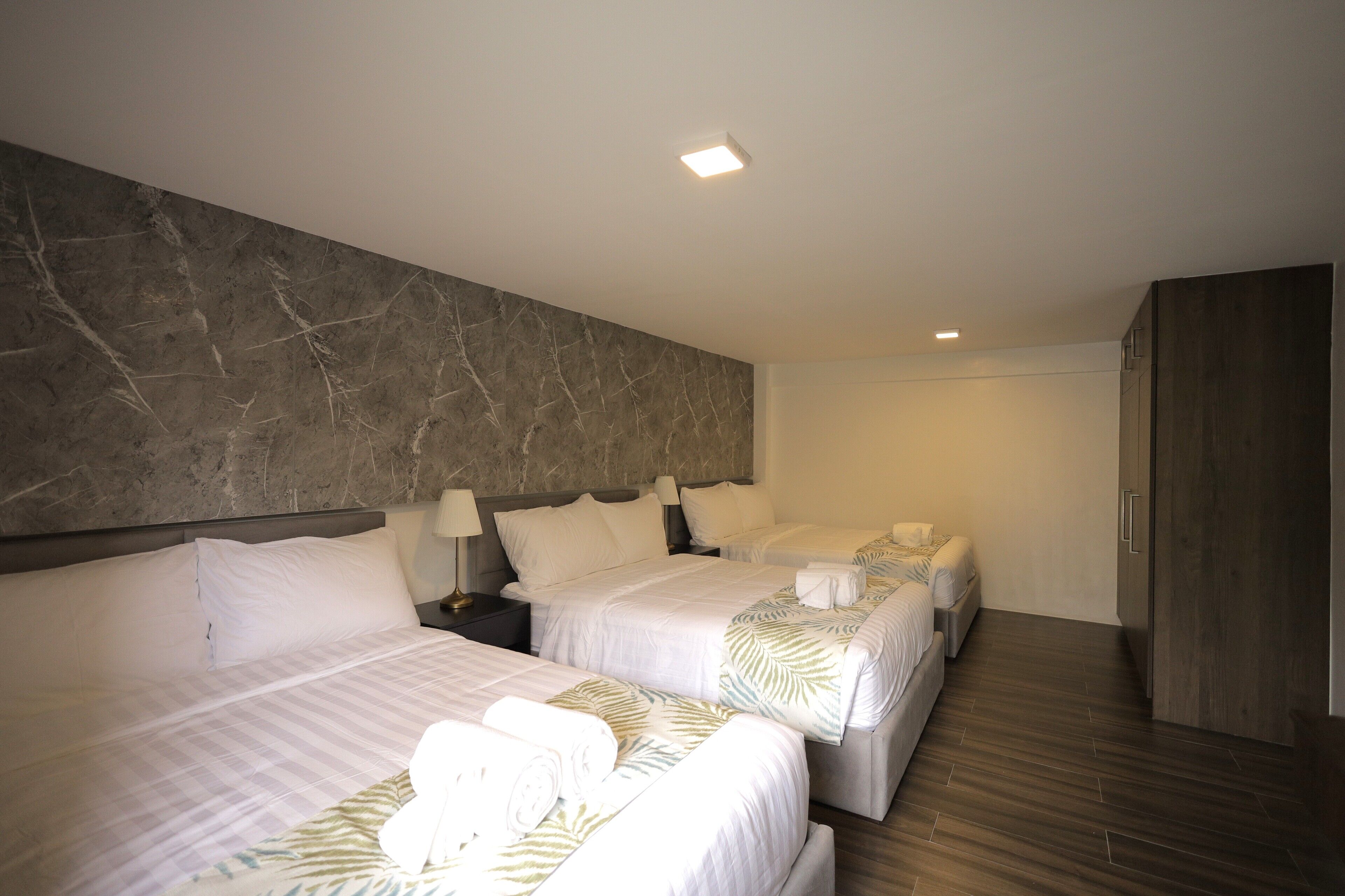 Ein Hotelzimmer mit zwei Betten, einem Marmorkopfstück, einem Kleiderschrank und einem Nachttisch mit Lampe.