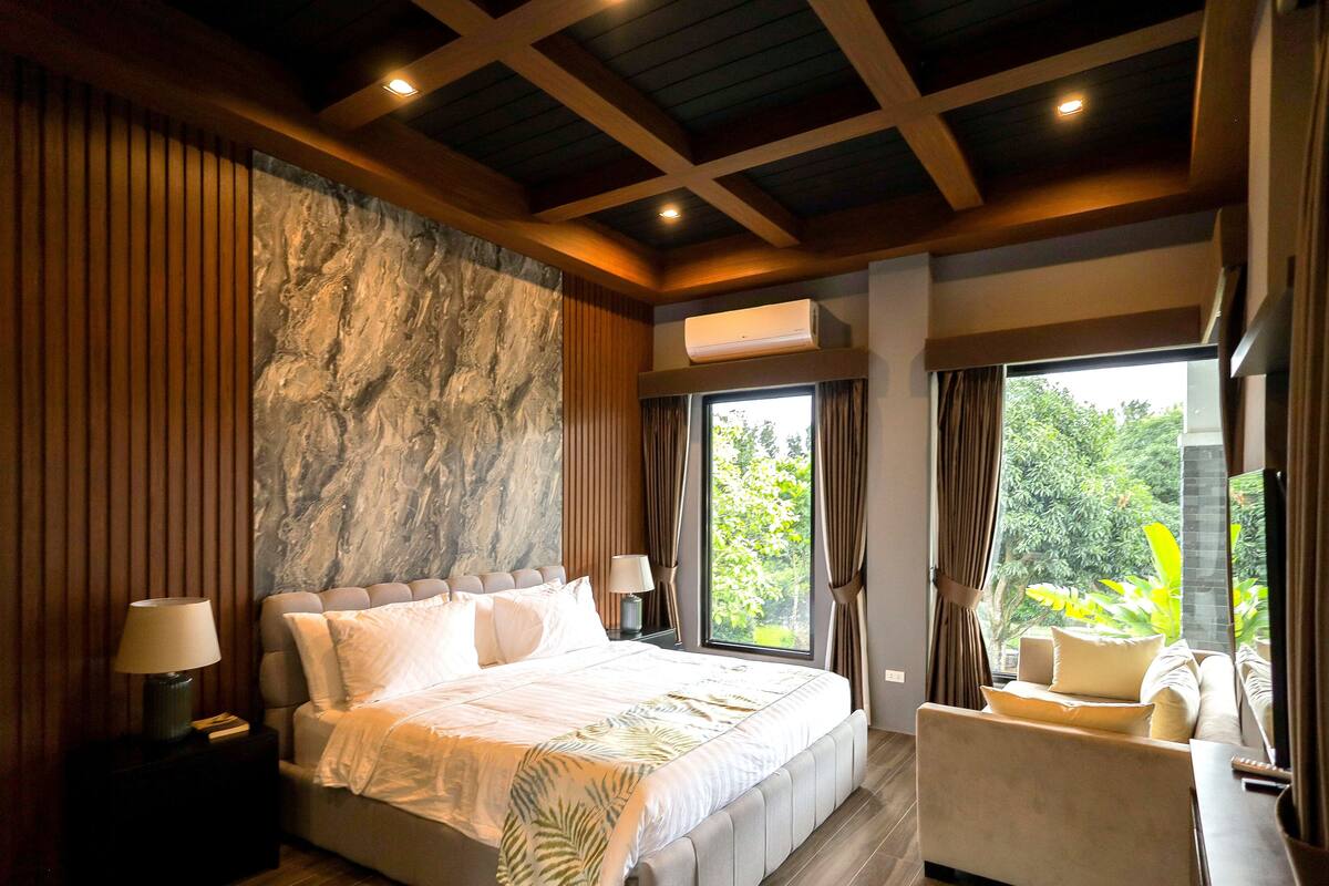 A spacious bedroom with a large bed, a sitting area, and a view of greenery outside.