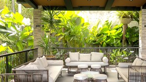 An outdoor patio area with a sofa set and round tables, surrounded by lush green plants. - Likha Wellness Resort (Lipa)