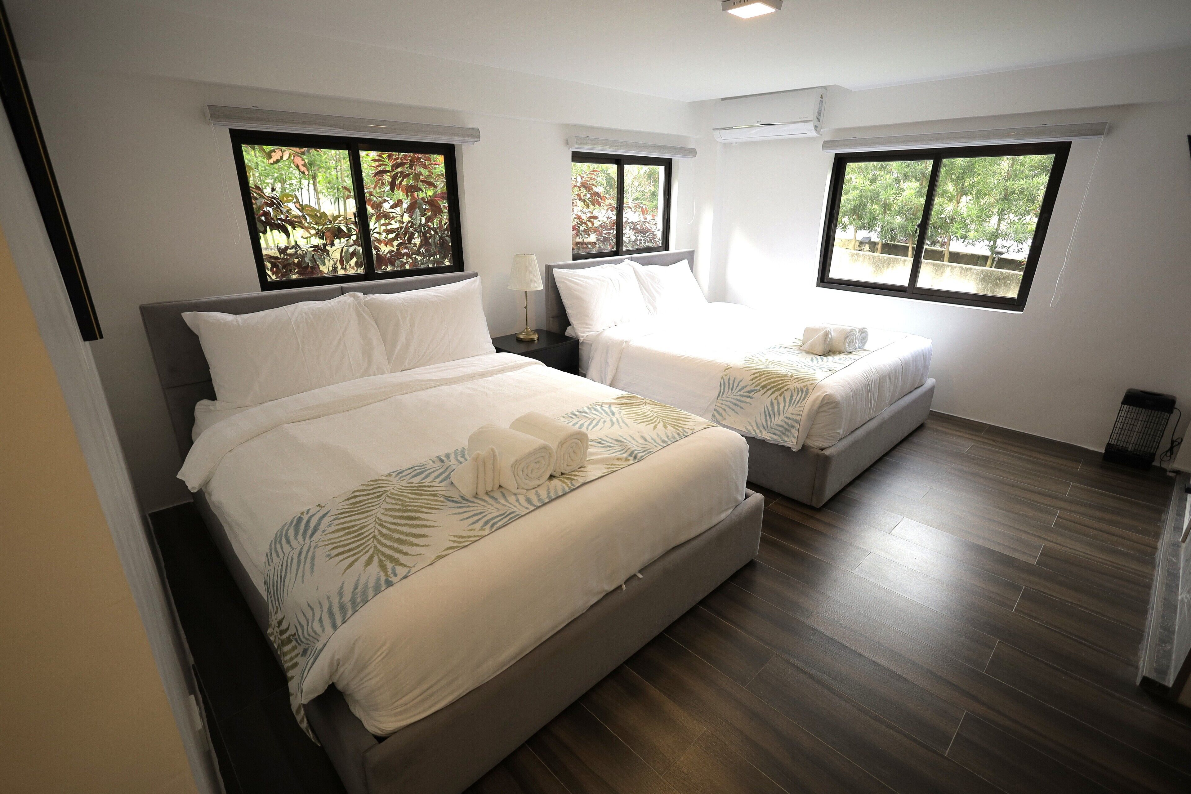 Habitación de hotel con dos camas, ventanas amplias y suelo de madera.