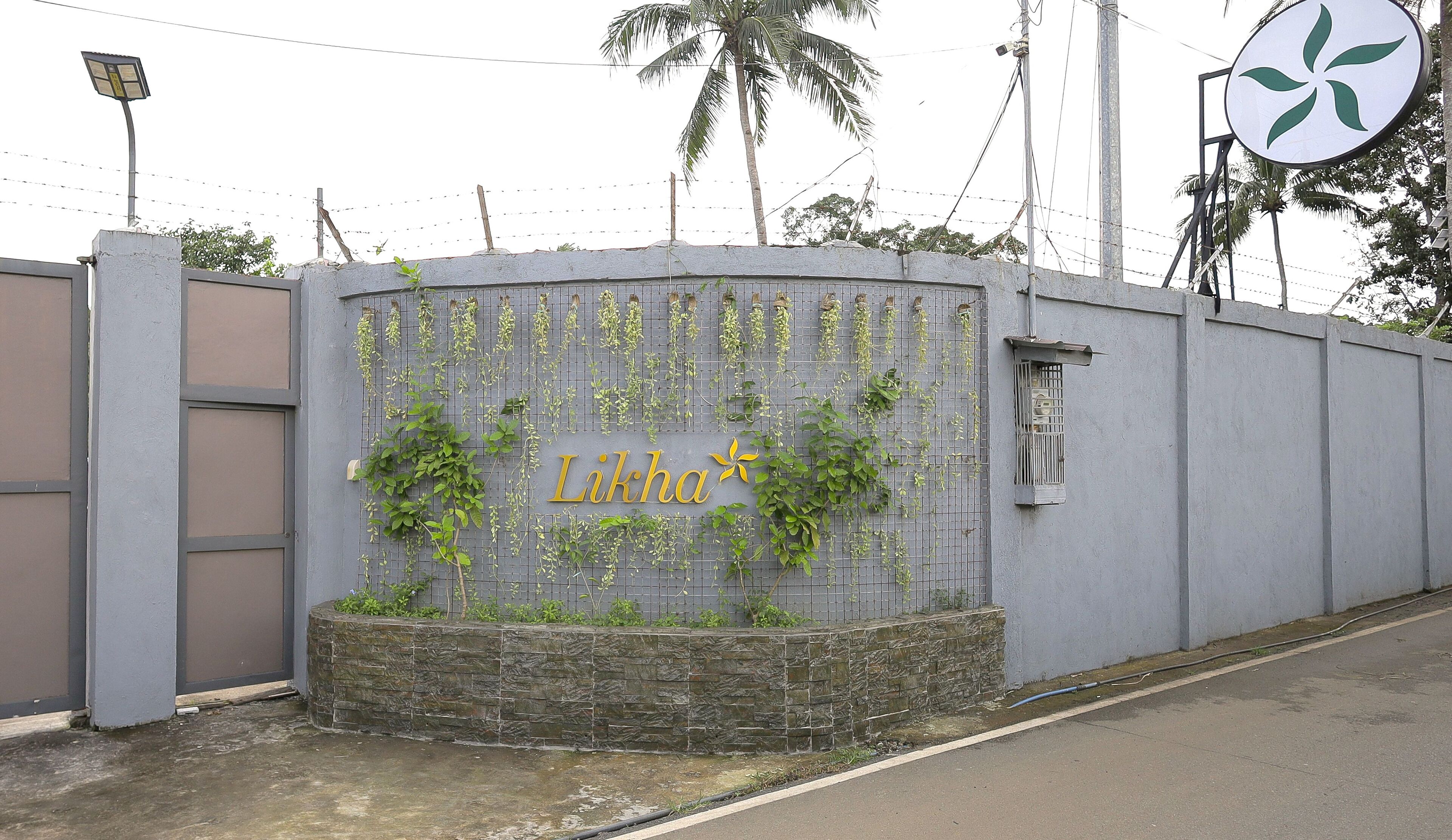 A grey wall with the name 'Likha' in gold lettering, surrounded by climbing plants.