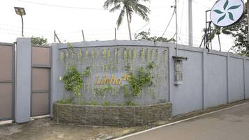 A grey wall with the name 'Likha' in gold lettering, surrounded by climbing plants.