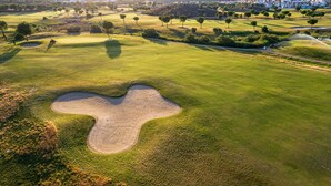 A golf course with sand bunkers, trees, and a distant residential area.