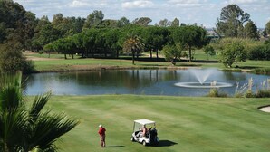 A golf course with a pond, trees, and a golf cart.