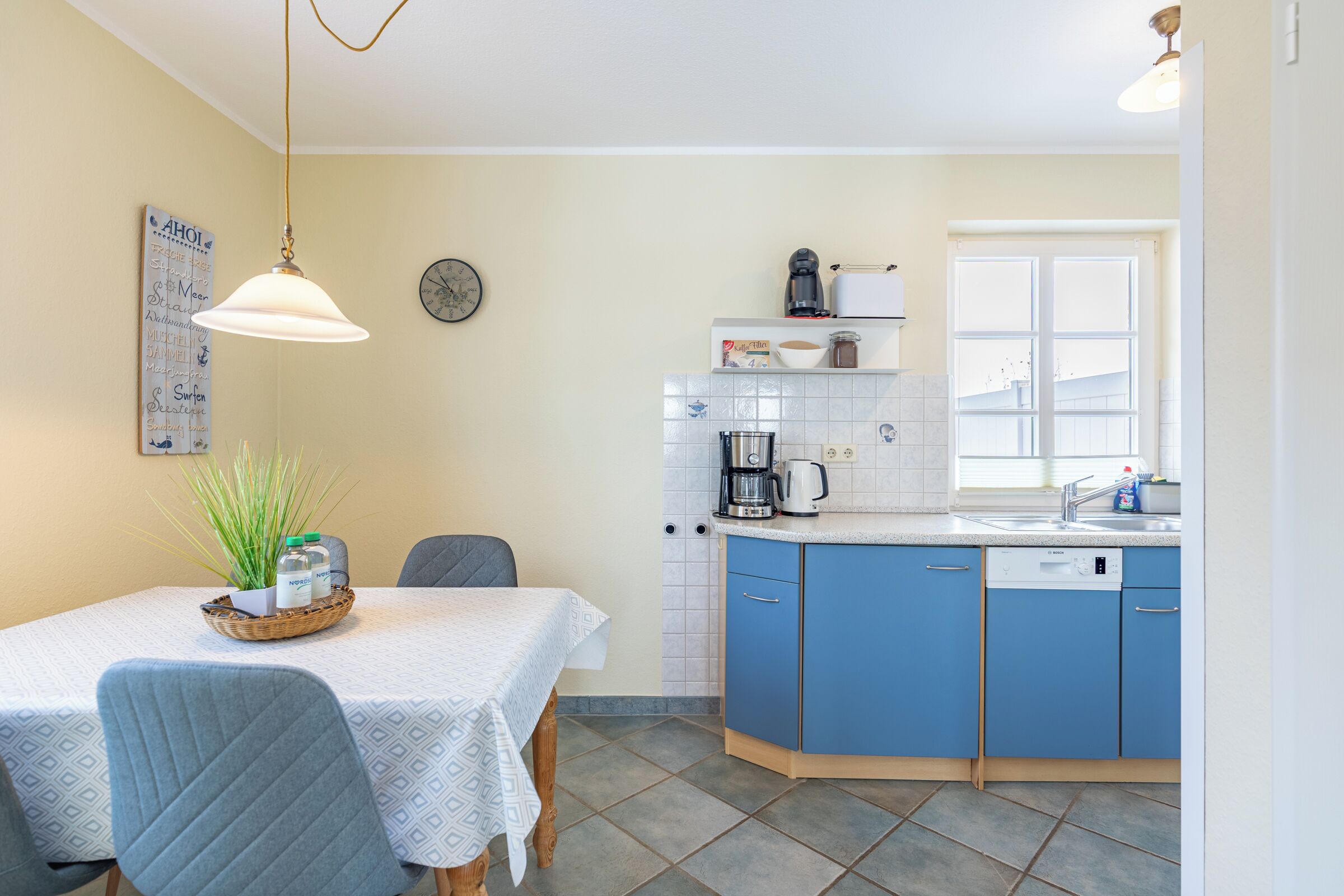 A compact kitchen with blue cabinets, a white countertop, and a dining area with a table and chairs.
