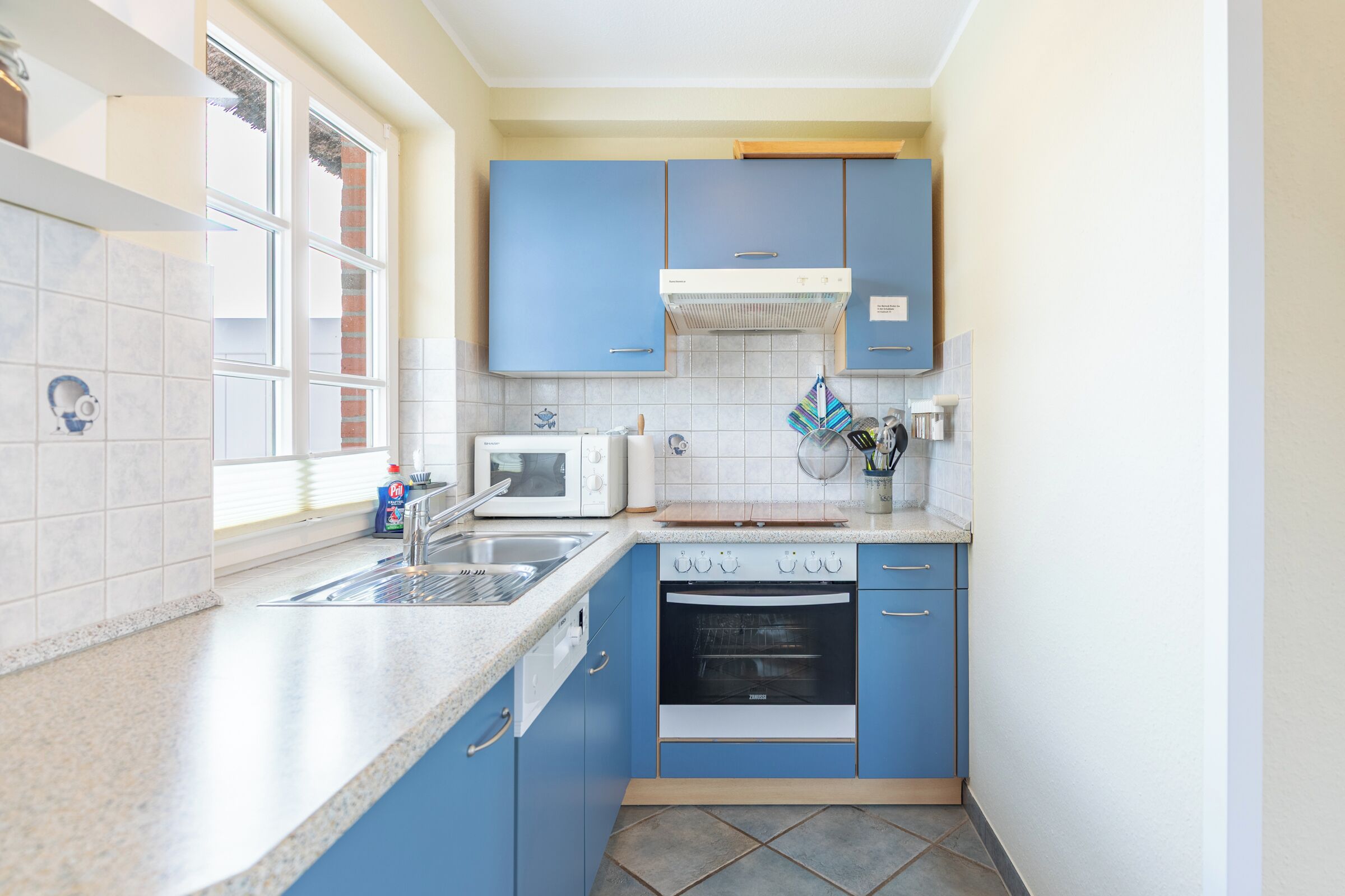 A compact kitchen with blue cabinets, a microwave, an oven, and a sink.