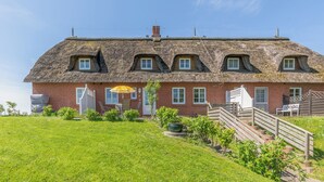 Ett traditionellt hus byggt av tegel med ett halmtak, en ytterdörr och en trappa som leder upp till en träveranda.