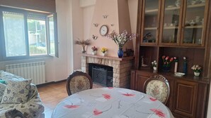 A cozy living room with a fireplace, a dining table with a floral tablecloth, and a china cabinet. - Large and bright apartment in residential area, 6 bus stops from metro A (Roma)