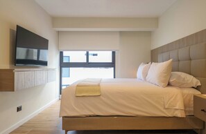 Moderni hotellihuone, jossa on suuri sänky, seinälle asennettu taulutelevisio ja ikkuna, josta avautuu näkymä kaupunkiin.