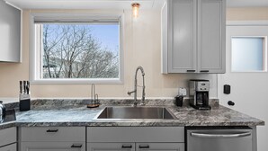 A kitchen with a large window, a stainless steel sink, a coffee maker, and a dish rack.