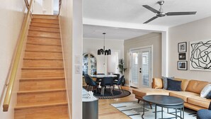 A staircase leading to a dining area with a round table and chairs, a sofa, and a ceiling fan in a modern living space.