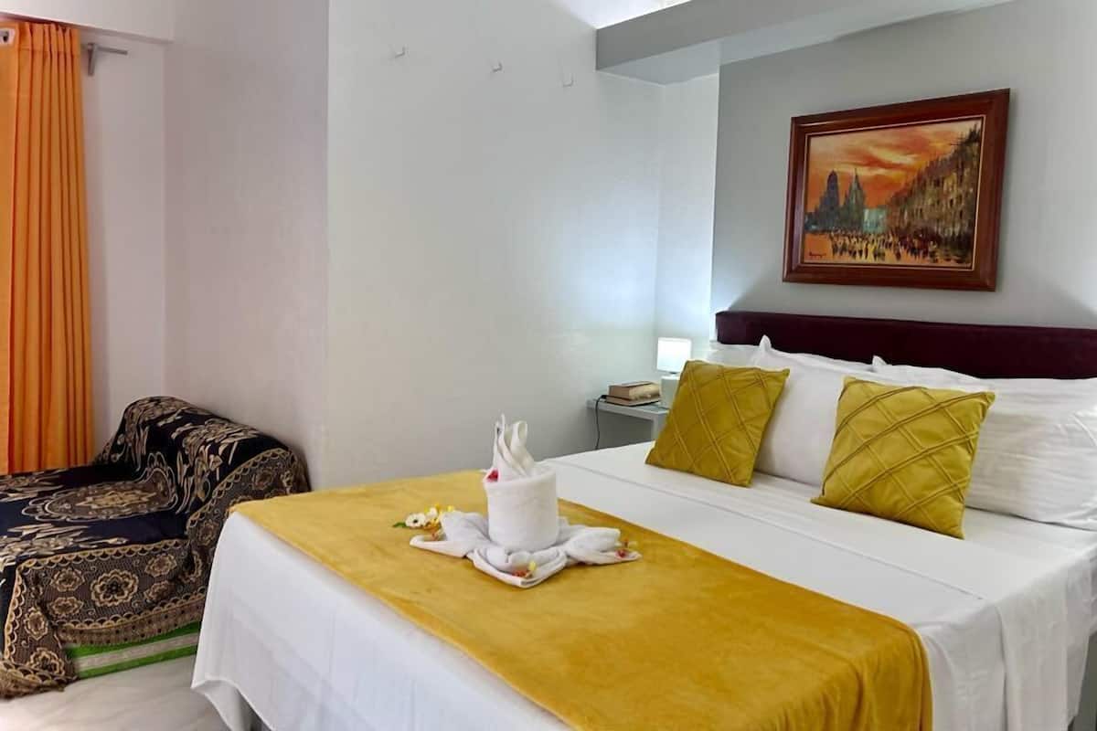 Quarto de hotel com cama, mesa de cabeceira, quadro e cadeira.