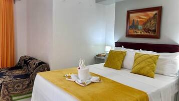 Una habitación de hotel con cama, mesita de noche, un cuadro y una silla.