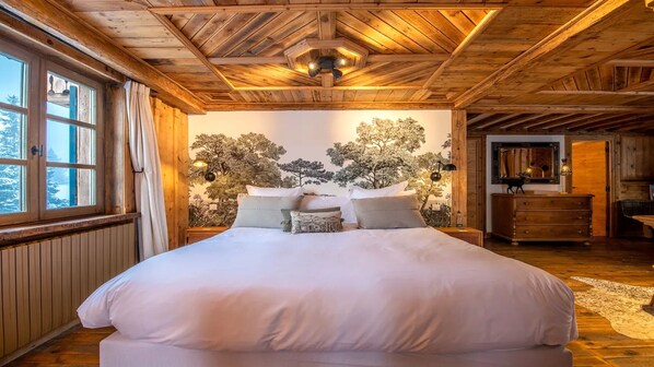 A bedroom with a large bed, wooden ceiling, and a wall mural of trees. - Fantastique mansarde appartement (Zermatt)