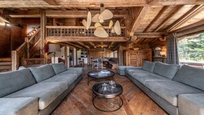 A rustic wooden interior with a high ceiling, two grey sofas facing a central coffee table, and a dining area in the background. - Fantastique mansarde appartement (Zermatt)
