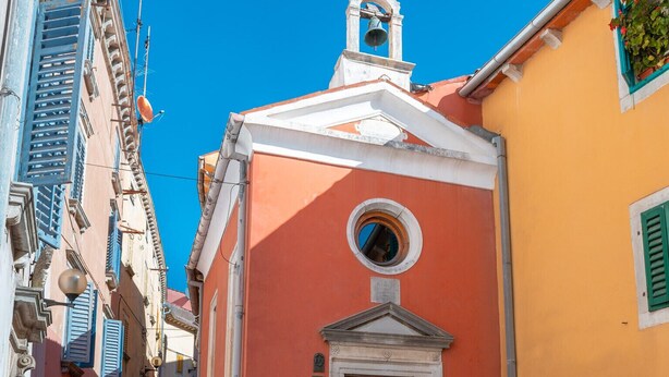 A narrow cobblestone street with a building featuring a wooden door and a bell tower.