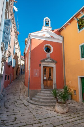 Una estrecha calle adoquinada con un edificio que tiene una puerta de madera y una torre de campanas.