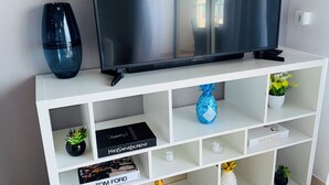 A white entertainment unit with a flat-screen TV, a blue vase, and various decorative items including books and small potted plants. - Beachfront Condo on Boardwalk – 2BR/2BA with Views (Philipsburg)