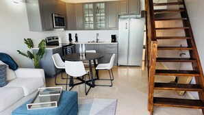 A modern kitchen with grey cabinets, a stainless steel refrigerator, and a dining area with a round table and white chairs. - Beachfront Condo on Boardwalk – 2BR/2BA with Views (Philipsburg)