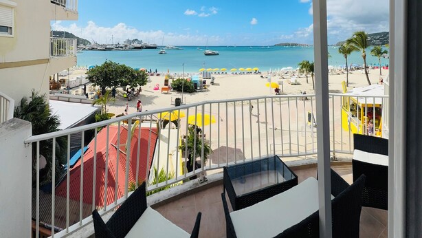 A balcony with a view of a beach, a marina, and a clear sky. - Beachfront Condo on Boardwalk – 2BR/2BA with Views (Philipsburg)