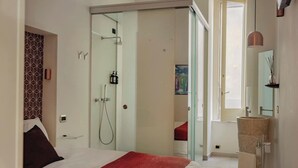 A modern hotel room with a bed, a glass shower enclosure, a sink, and a large window. - Da Celeste (Naples)