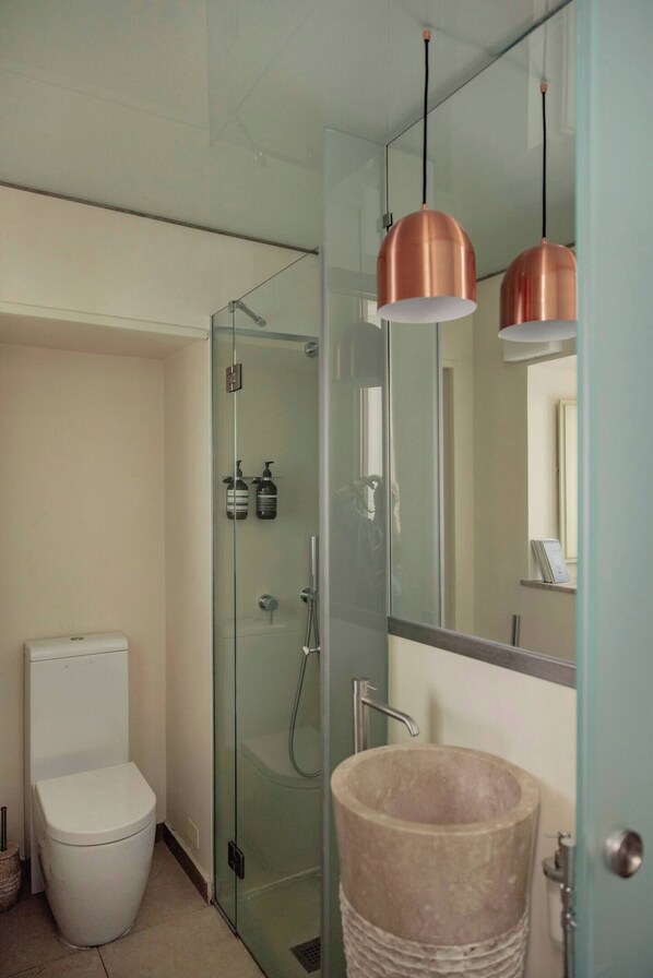 Ein modernes Badezimmer mit Duschkabine aus Glas, einer weißen Toilette und einem großzügigen Becken aus Stein.