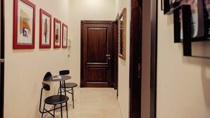 A narrow hallway with framed pictures on the walls, a wooden door at the end, and a small table with two chairs. - Da Celeste (Naples)