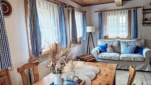 Ein gemütliches Wohnzimmer mit einem Holztisch, einer blauen Couch mit Kissen und einer Vase mit getrockneten Blumen.