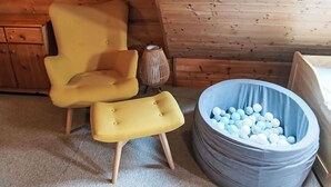 Ein Zimmer mit Holzboden, einem gelben Sessel, passendem Hocker, einer kleinen Dekorationsvase und einem blauen Ballbecken.