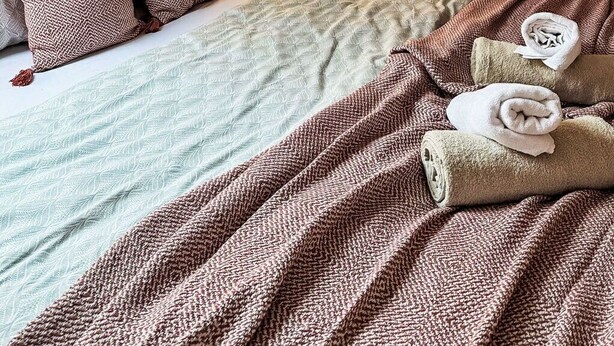 Ein gemütliches Schlafzimmer mit schrägem Dach, einem Bett mit gemusterten Betttextilien, einer Nachttischlampe und einem Nachttisch mit einer Vase mit Ästen.