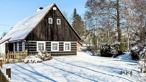 Ein hölzernes Bauernhaus mit geneigtem Dach, umgeben von schneebedecktem Boden und Bäumen.