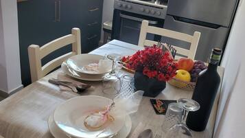 A dining table set with plates, cutlery, and a bottle of water, with a kitchen in the background.
