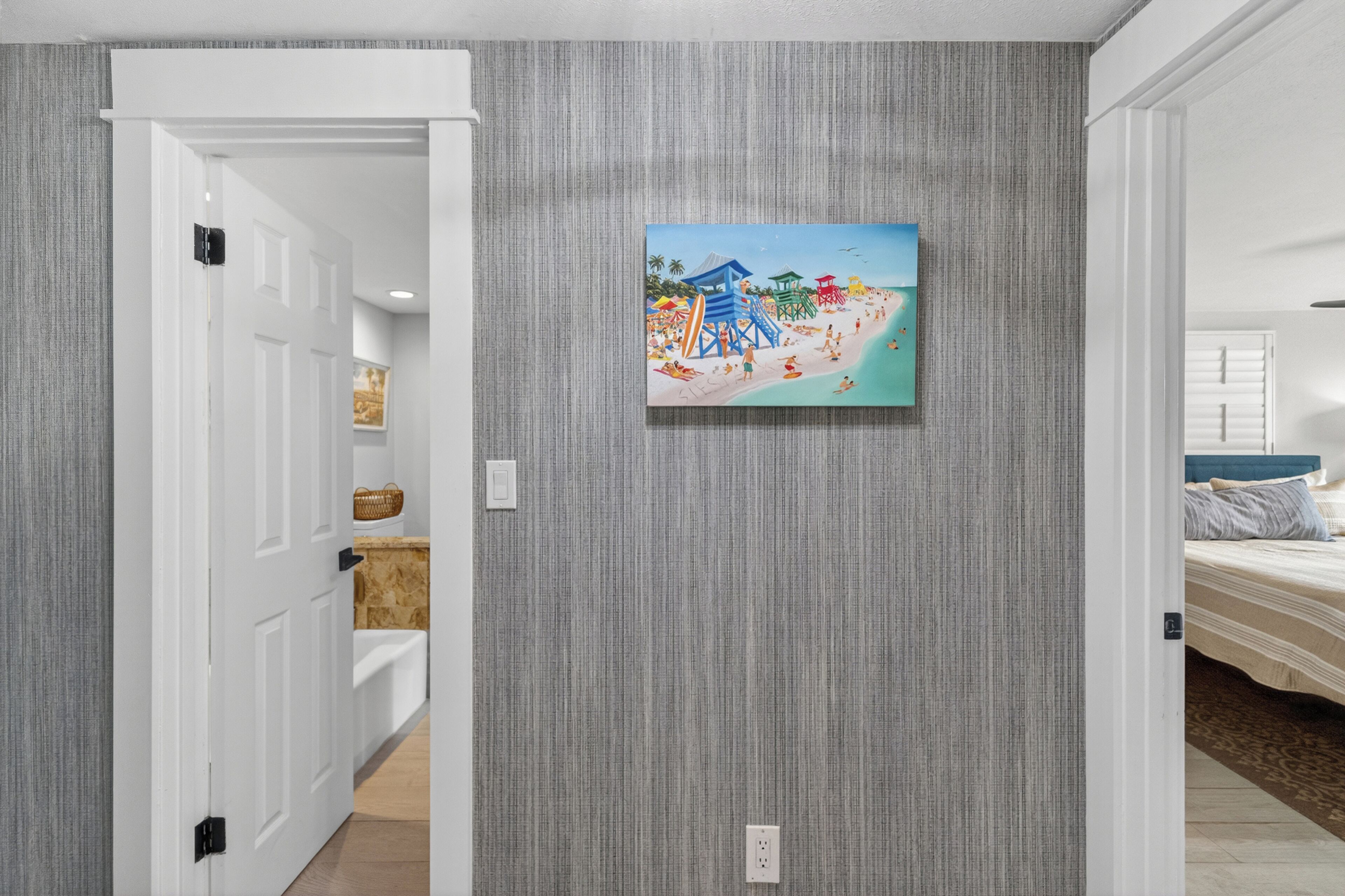 Ein Flur mit einer strukturierten grauen Wand, einer zur Zimmerführenden Tür und einem Strandbild.