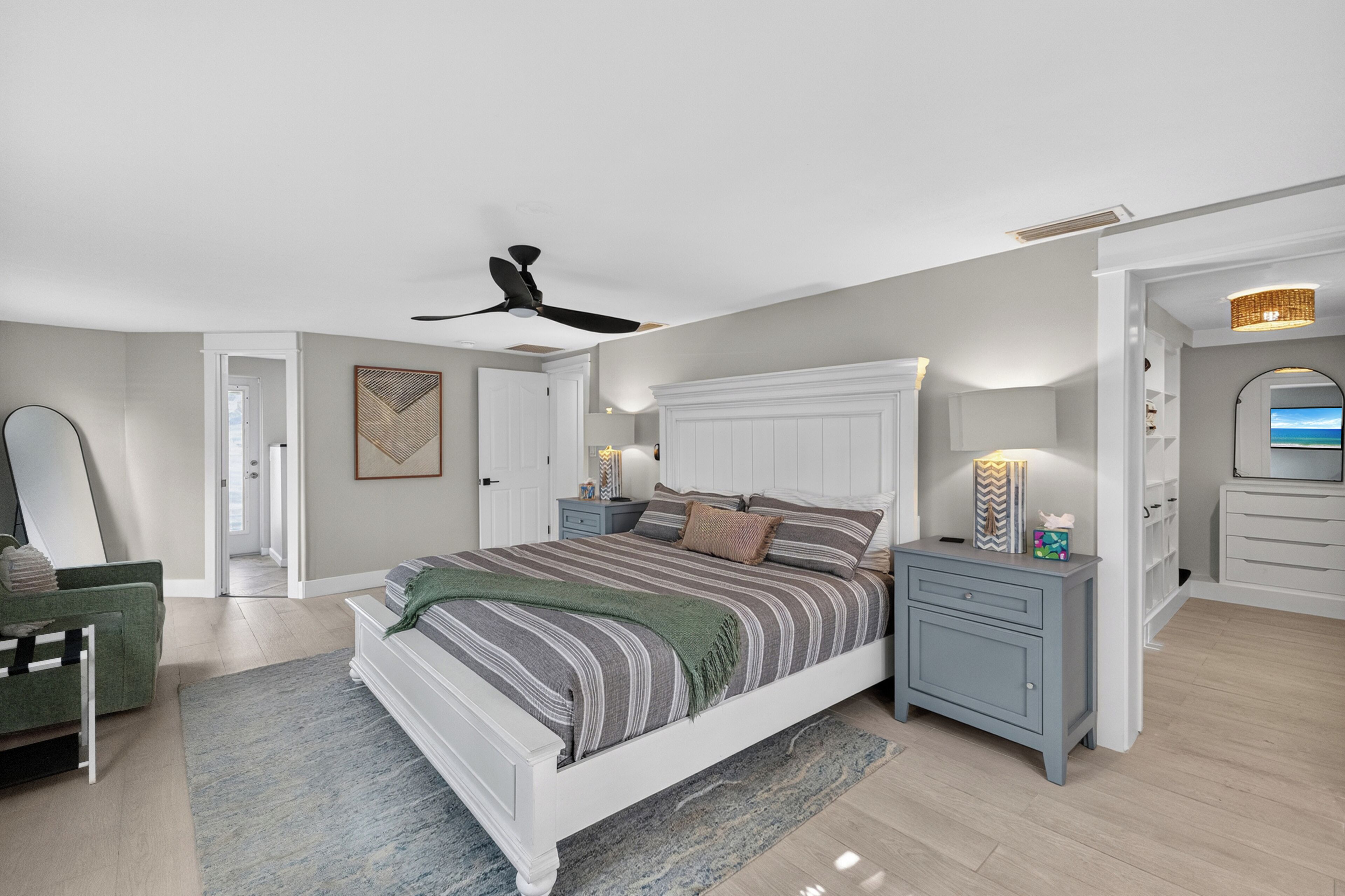 Un dormitorio con cama, mesitas de noche, cómoda, ventilador de techo y puerta que da a otra habitación.