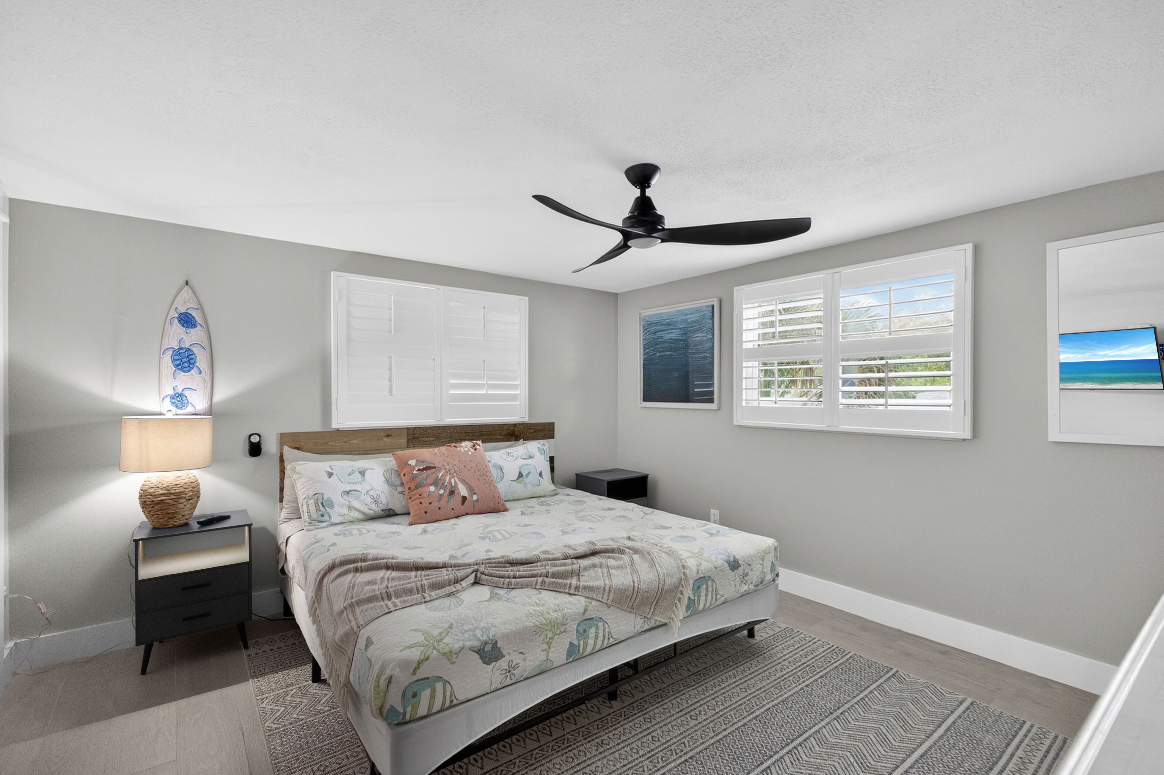A bedroom with a bed, a nightstand, a lamp, a ceiling fan, and a window with blinds.