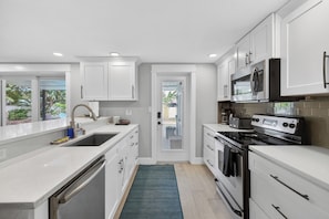 A modern kitchen with white cabinetry, stainless steel appliances, and a view through a glass door. - Luxury Pool Retreat near Siesta Key  (Sarasota)