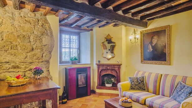 Un salon chaleureux avec un mur en pierre, une cheminée, un canapé à rayures et une table en bois ornée de fruits et de fleurs.