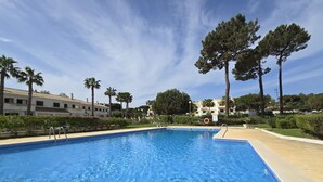 A swimming pool with clear blue water, surrounded by palm trees and a building with a tiled roof. - Beautiful private villa for 6 people with pool, WIFI, TV and patio (Praia Da Falesia)