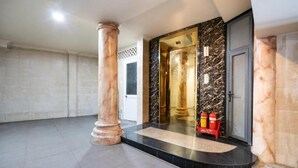 Vestíbulo de hotel con una columna de mármol, un mostrador de recepción y un extintor.