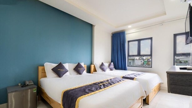 Habitación de hotel con dos camas, un escritorio, un refrigerador pequeño y una ventana con cortinas.