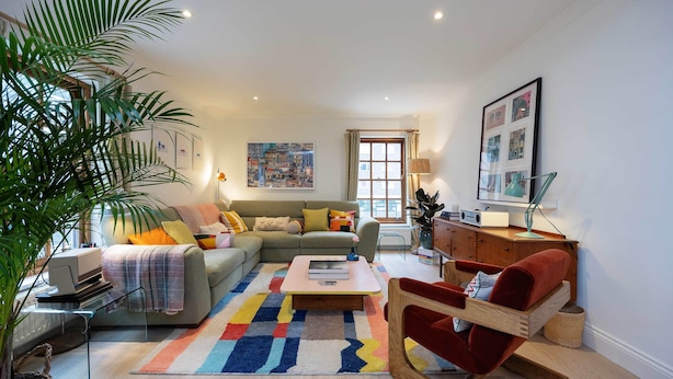 A modern living room with a sofa, a coffee table, a red chair, a large plant, and artwork on the walls. - The Lancaster Gate Mews House, by Veeve (London)