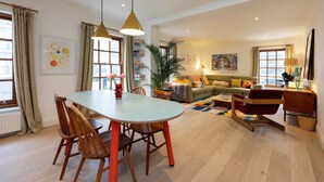 A modern living room with a dining table, chairs, a sofa, and a coffee table. There is a plant, books, and artwork on the walls. - The Lancaster Gate Mews House, by Veeve (London)
