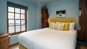 A bedroom with a large bed, a window with a view of buildings, a wooden bookshelf, and a painting on the wall. - The Lancaster Gate Mews House, by Veeve (London)
