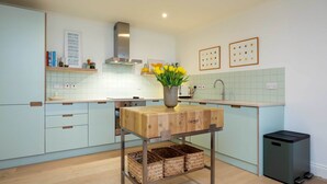 A modern kitchen with light blue cabinets, a wooden table with a vase of yellow flowers, and a black trash bin. - The Lancaster Gate Mews House, by Veeve (London)