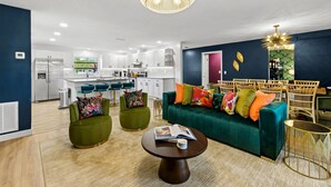 Ein modernes Wohnzimmer mit einem grünen Sofa, zwei Sesseln, einem Couchtisch und einem Essbereich mit einem Holztisch und Stühlen.