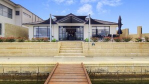 A modern house with a wooden dock leading to a water body, surrounded by a stone wall and a garden with flowers. - Canal Waters relax and enjoy even bring the boat to the back door (Geographe)