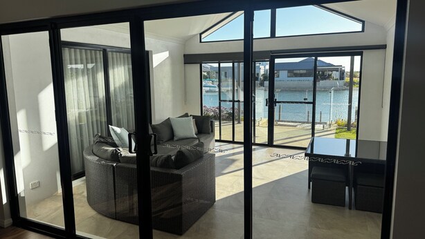 A modern living room with a large sliding glass door leading to a balcony with a view of a body of water. - Canal Waters relax and enjoy even bring the boat to the back door (Geographe)