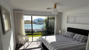 A bedroom with a large bed, a chair, a view of a body of water, and a ceiling fan. - Canal Waters relax and enjoy even bring the boat to the back door (Geographe)