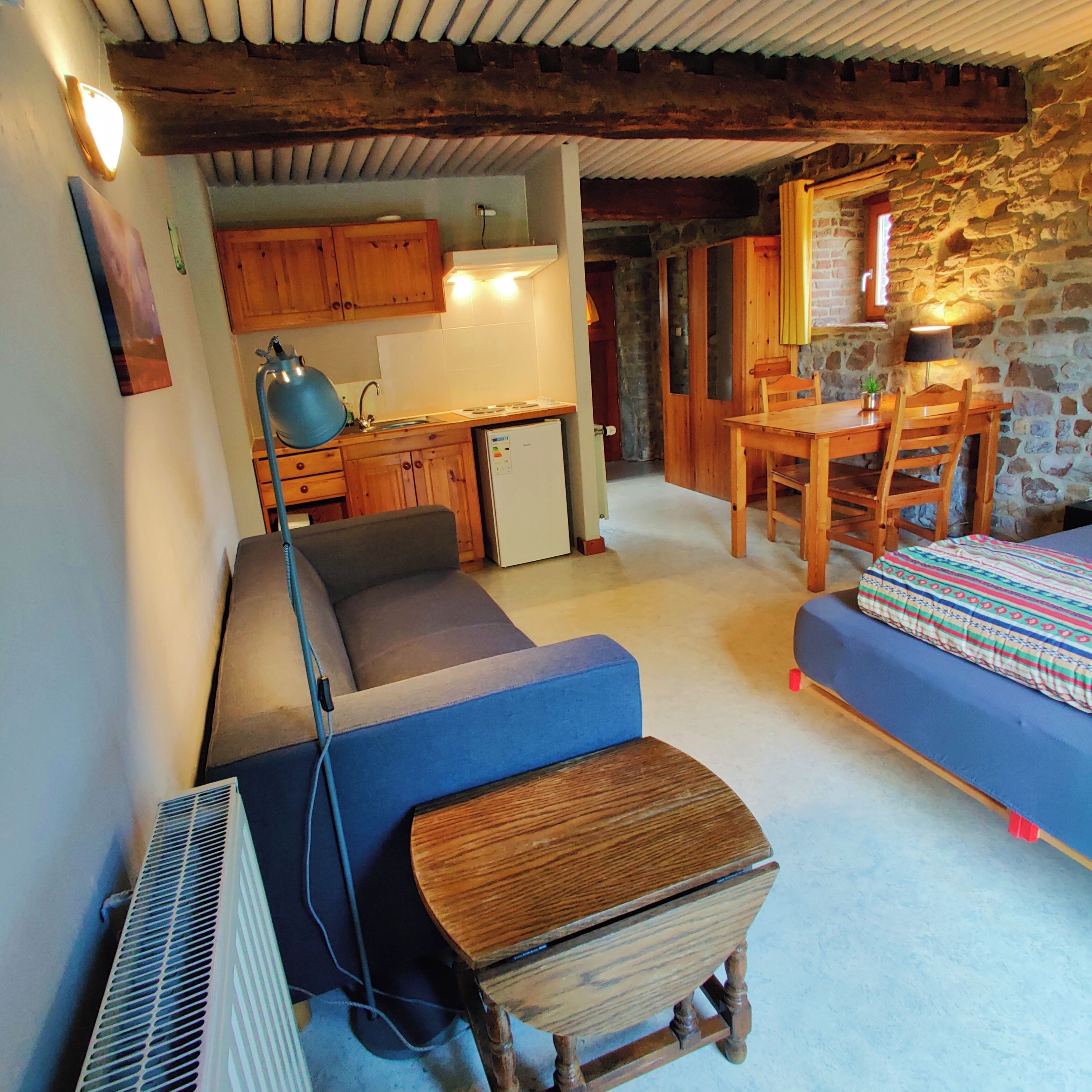 A cozy room with a sofa, a small wooden table, a bed, a desk, and a kitchenette.